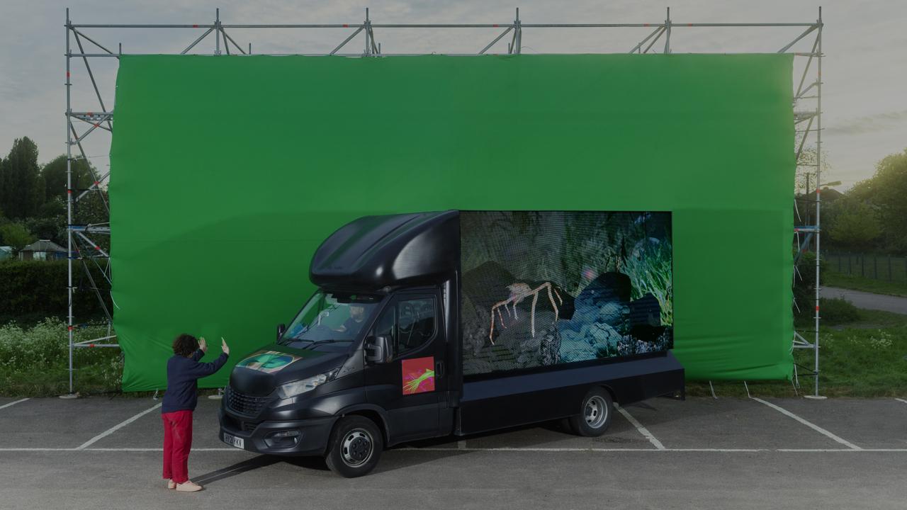 a woman stands in front of a black van with a screen on the side 